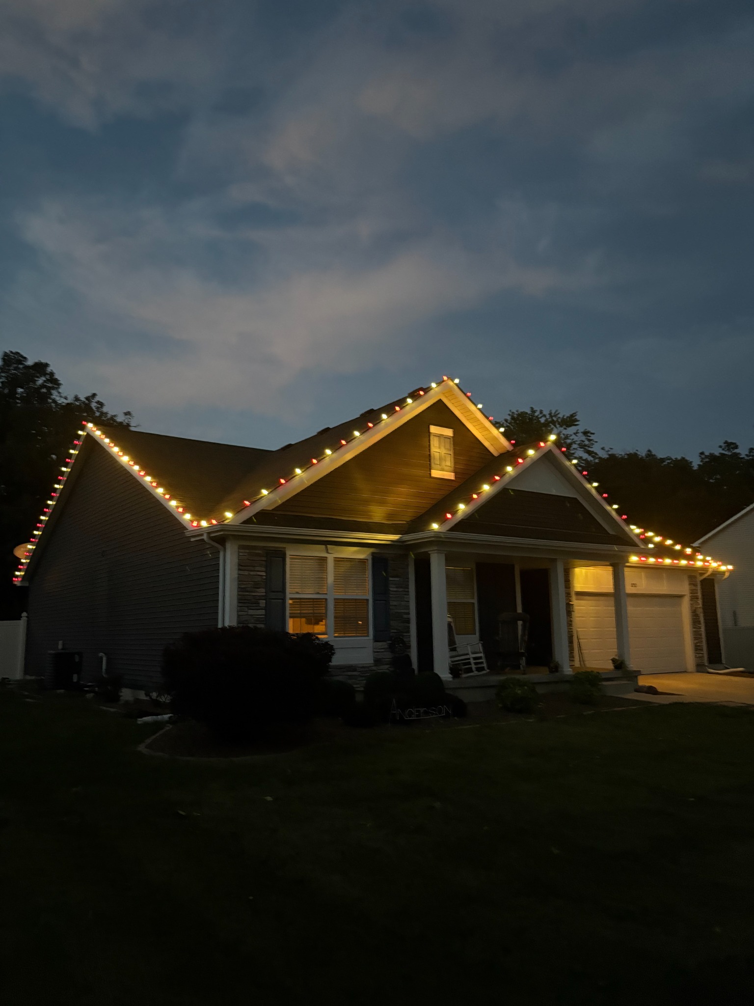 Residential home with custom red and warm white Christmas roofline lighting at dusk